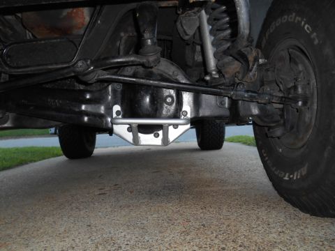 1994 Ford Bronco - The underside of a 1994 Ford Bronco shows the front differential, suspension components, and steering linkage. A silver aftermarket brace i…