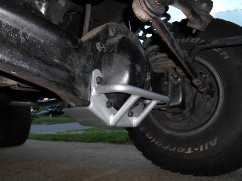 1994 Ford Bronco - A silver-painted skid plate is bolted to the underside of a black differential housing on a vehicle. The front tire with "All-Terrain T/A"…