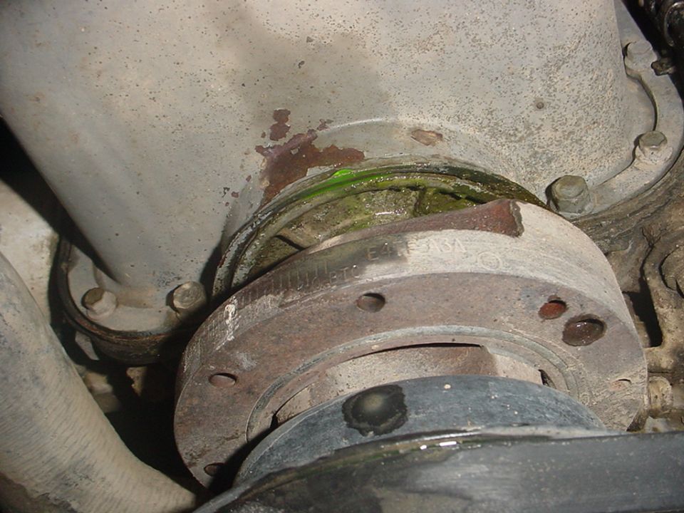 Green coolant seeping from a rusty water pump housing seam above the crank pulley