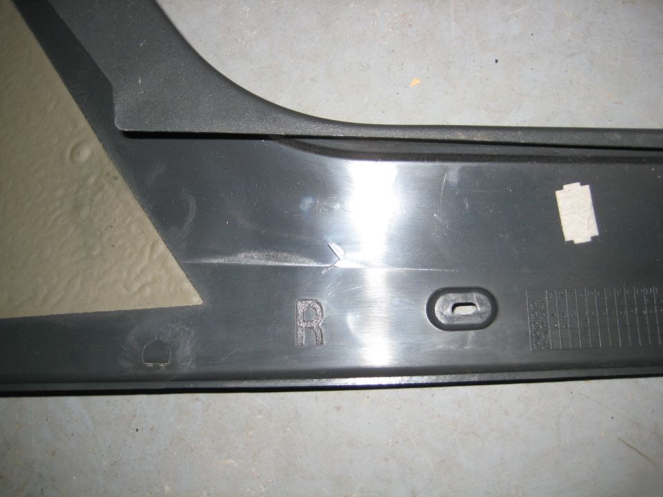 Black plastic trim piece with an embossed 'R' and a small oval cutout.