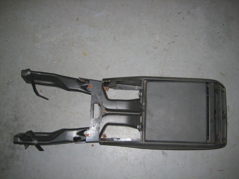 Black plastic center console assembly on gray concrete floor.