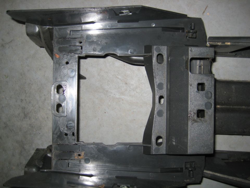 Black plastic automotive part with a central rectangular opening and mounting holes.