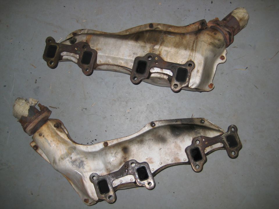 Two used metal exhaust manifolds on a concrete floor