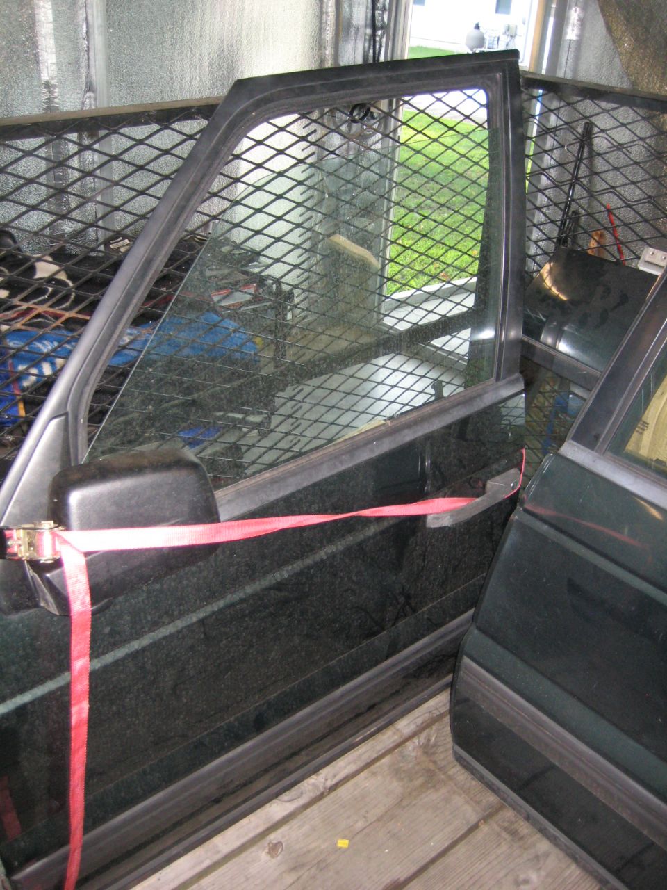 Dark green Range Rover door open and secured with red strap, diamond plate barrier inside.