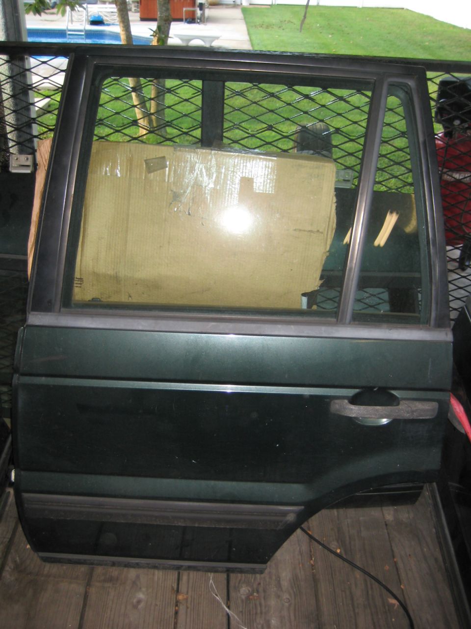 Dark green Range Rover rear door with window showing a cardboard box, detached and on wooden planks.