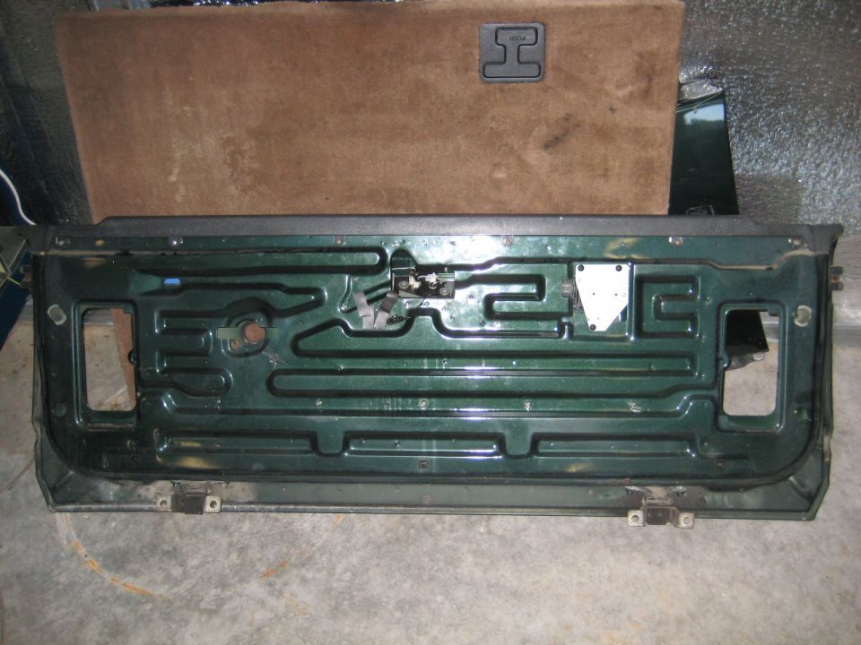 Interior of a dark green tailgate with visible internal structure and latching mechanism. Brown carpeted panel above.
