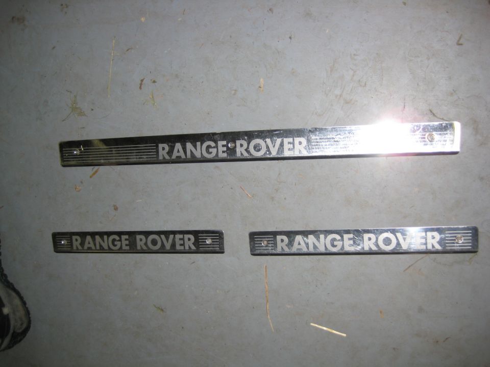 Three chrome Range Rover emblems on a gray surface.