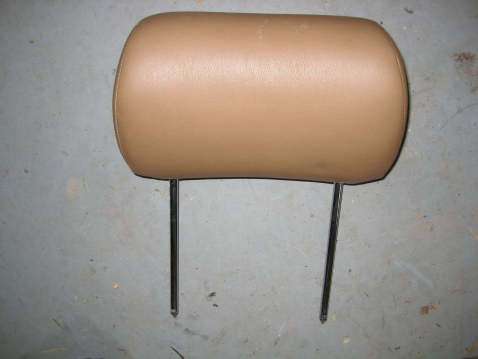 Tan leather car headrest with chrome posts on a concrete floor.