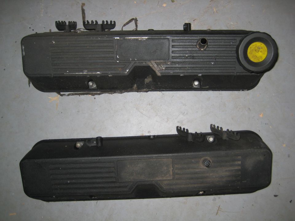 Two black valve covers on a gray concrete surface. One has a yellow cap.