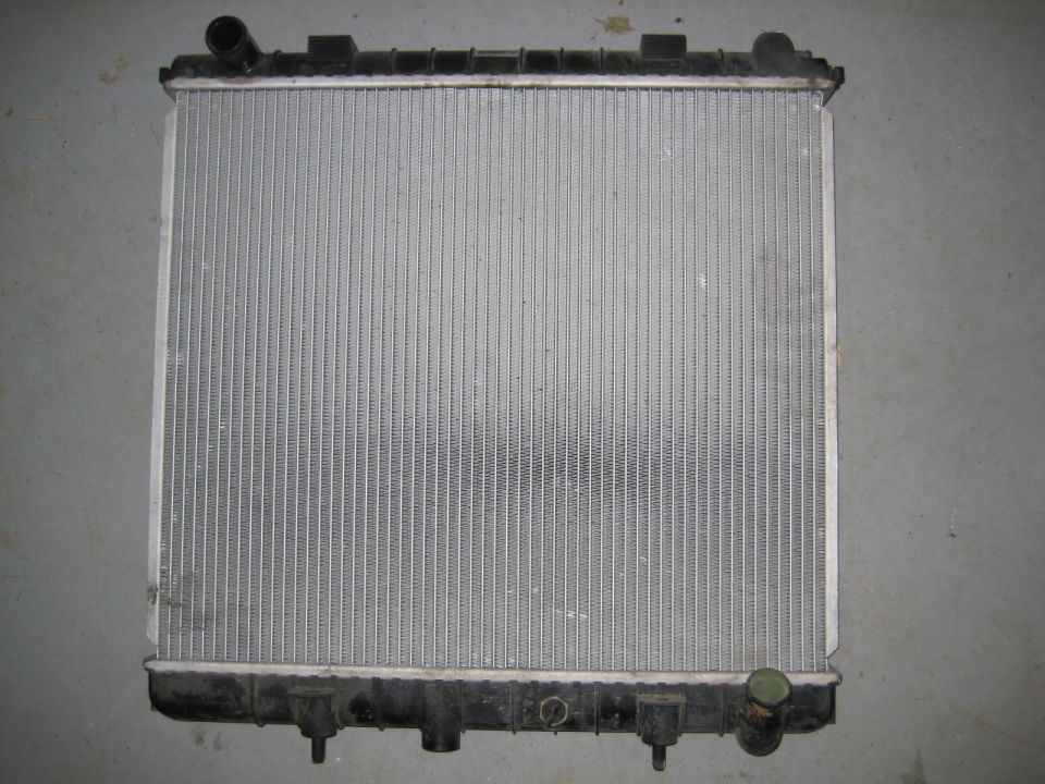Vehicle radiator with aluminum fins and black plastic tanks.