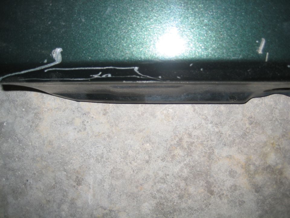 Close-up of dark green vehicle body panel with black trim and white markings.