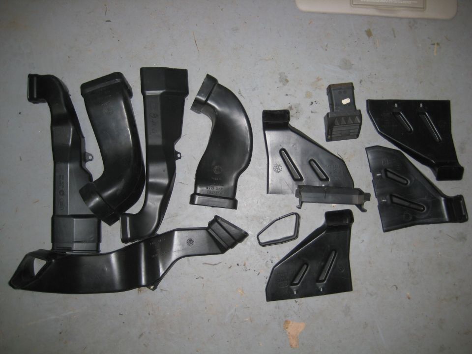 Assorted black plastic automotive air ducting and trim pieces on a concrete floor.