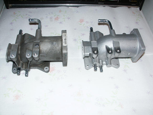 Two aluminum throttle body castings with coolant tubes compared side by side