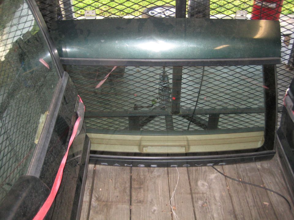 Dark green Land Rover Range Rover tailgate with rear window on wooden planks.