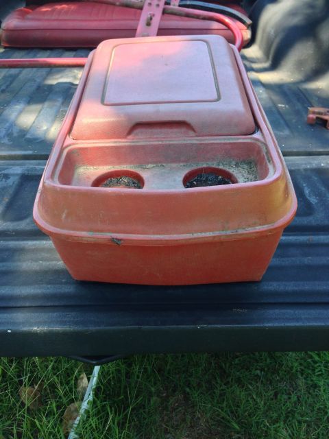 1979 Ford Bronco - A red plastic console with two cup holders sits on the tailgate of a dark-colored truck. The console has a hinged lid and appears to be a p…