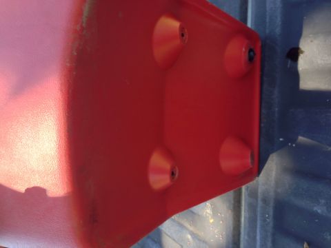 1979 Ford Bronco - A close-up view of the underside of a red plastic part, possibly a fender or body panel, with four conical protrusions. The part is resting…