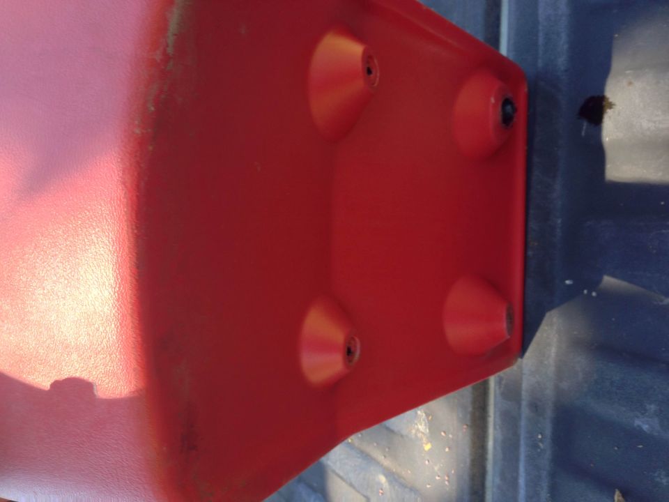 Red plastic vehicle part with conical protrusions on a dark blue surface.