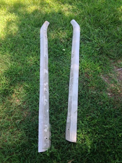 1979 Ford Bronco - Two silver metal trim pieces are laid out on a grassy lawn. The pieces are curved and appear to be part of a vehicle's exterior trim.