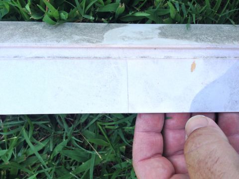 1979 Ford Bronco - A close-up shot shows a person's hand holding a piece of trim or molding against a background of green grass. The trim is light-colored wit…