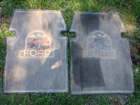 1979 Ford Bronco - Two grey Ford floor mats with a vintage red Ford Bronco graphic and the word "FORD" are laid out on the grass.