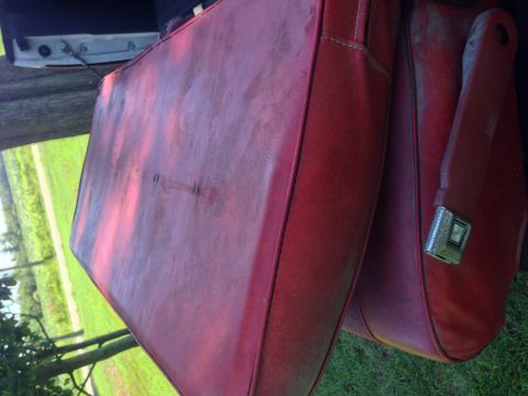 1979 Ford Bronco - A close-up, angled view of the red vinyl interior of a vintage vehicle, showing a seat cushion and a seatbelt buckle. The seat appears worn…