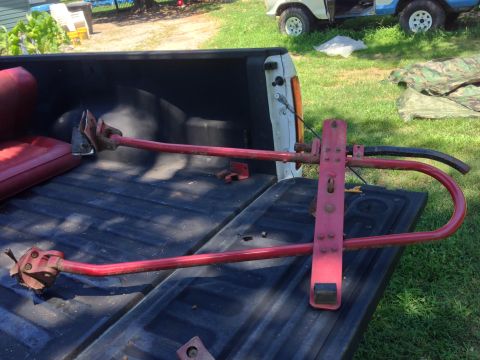 1979 Ford Bronco - A red metal trailer hitch assembly is laid out in the bed of a dark-colored pickup truck. The assembly includes a U-shaped bar and a vertic…