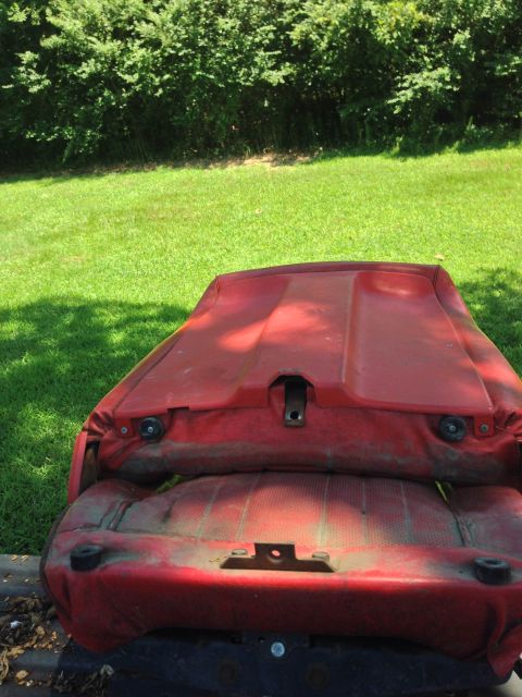 1979 Ford Bronco - The red plastic and fabric seat from a vehicle is shown outdoors, resting on a dark base. The seat is dirty and weathered, with visible mou…