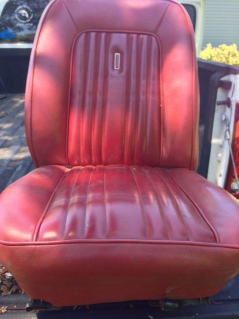 1979 Ford Bronco - A red vinyl bucket seat is shown from the front, likely from a classic SUV or truck. The seat has vertical pleating on the backrest and a h…