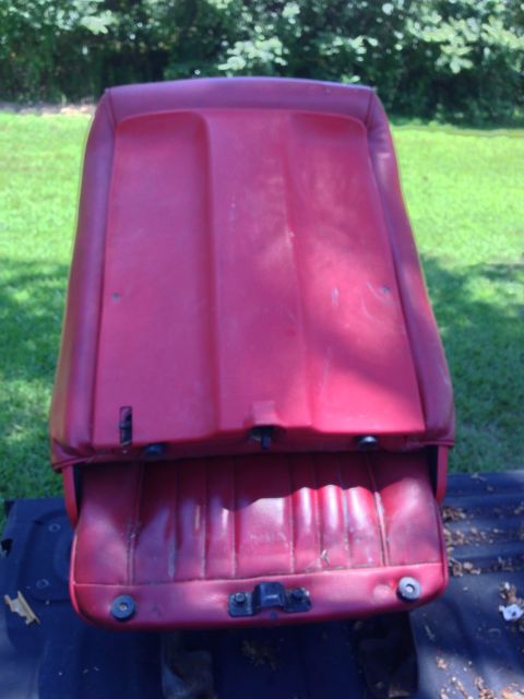 1979 Ford Bronco - A red vinyl car seat is shown from a top-down perspective, resting on a dark surface outdoors. The seat appears to be from an older vehicle…