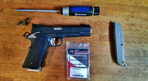 1996 Ford Bronco - A disassembled firearm is laid out on a wooden surface next to a utility knife and a screwdriver. The firearm appears to be a 1911 style pi…