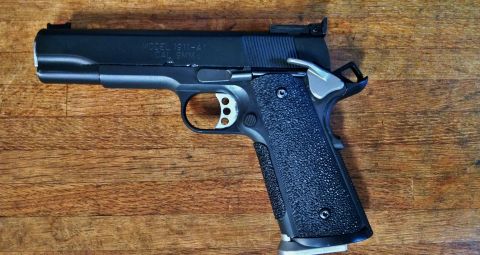 1996 Ford Bronco - A black semi-automatic pistol with textured grips rests on a wooden surface. The pistol appears to be a Model 1911-A1 chambered in 9mm.