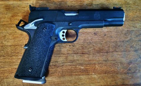 1996 Ford Bronco - A black Springfield Armory 1911 pistol with textured grips rests on a wooden surface. The slide is engraved with "SPRINGFIELD ARMORY" and o…