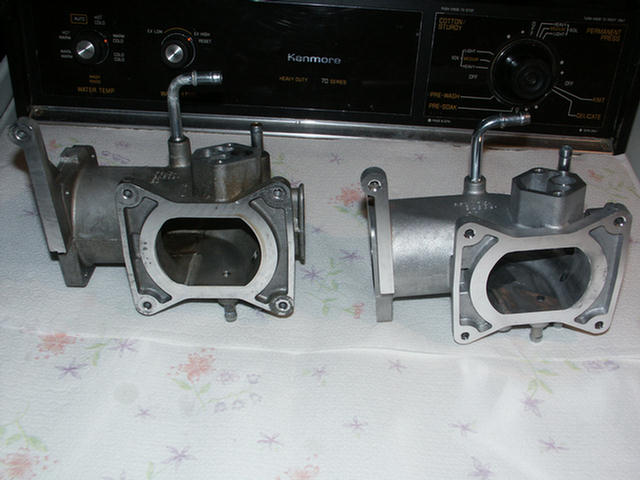 Two aluminum dual-bore throttle bodies compared side by side on a washer top