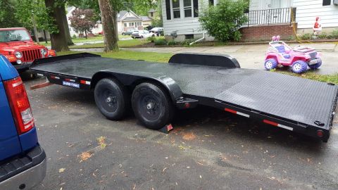 1994 Ford Bronco - A black Sure-Trac tandem-axle steel car hauler trailer parked in a residential driveway with its tilt deck angled down at the rear. The dia…