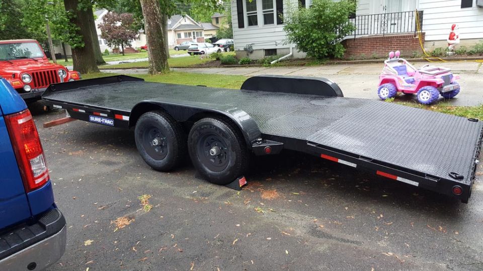 Black Sure-Trac tandem-axle tilt-deck car hauler trailer in a driveway