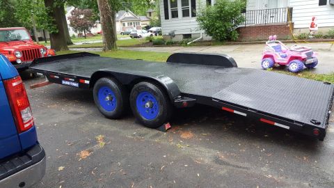 1994 Ford Bronco - A black Sure-Trac car hauler trailer with blue wheels is parked on a wet asphalt driveway. A red Jeep Wrangler is partially visible to the…