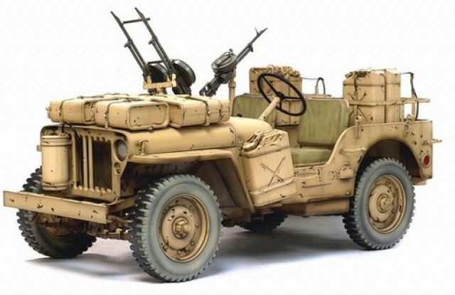 Desert tan open military Jeep with mounted machine guns, stowage bags and jerry cans, front three-quarter view