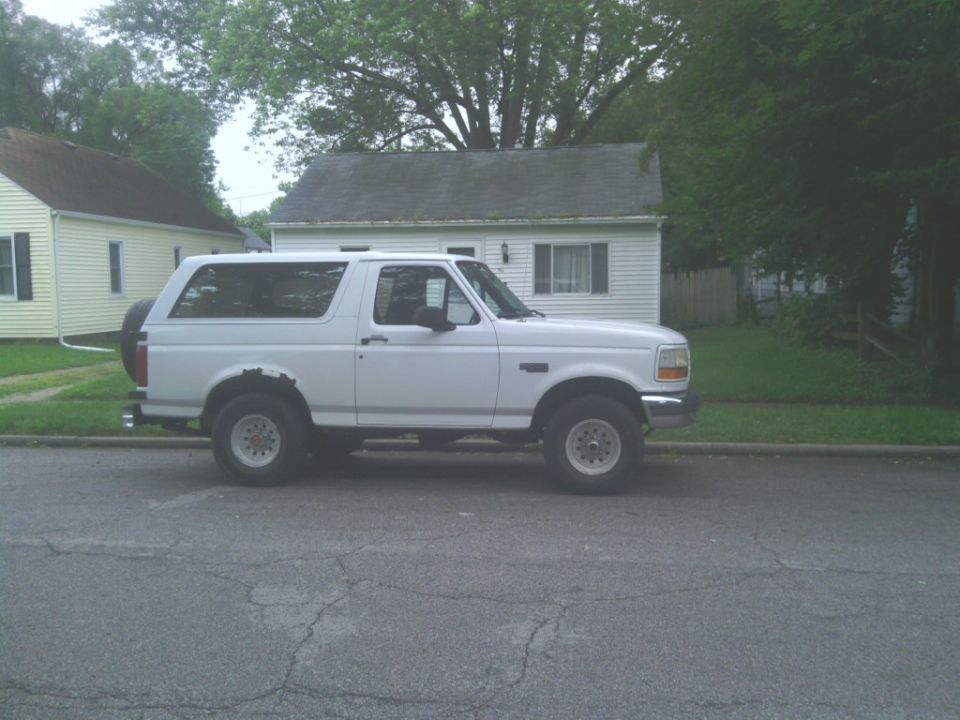 White two-door Ford Bronco SUV parked on a street, passenger side view, rust on rear fender