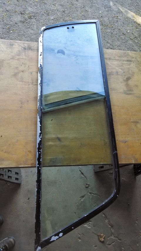 1992 Ford Bronco - A disassembled vehicle window with a black frame rests on a wooden surface. The glass is dirty and shows reflections of the sky and a woode…