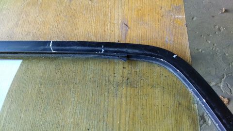 1992 Ford Bronco - A close-up view of a damaged black rubber seal and glass edge, likely from a vehicle window, resting on a wooden surface.