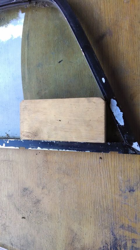 1992 Ford Bronco - A wooden block is placed on the edge of a car window frame, which is black with chipped paint. The background is a wooden surface.