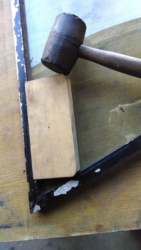 1992 Ford Bronco - A wooden block is placed on the edge of a black metal frame with peeling white paint, next to a large rubber mallet. The frame appears to b…