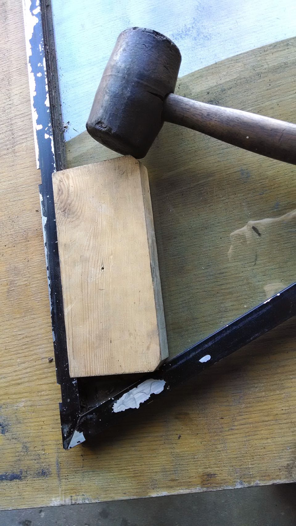 Wooden block and rubber mallet on a black metal frame with peeling paint.