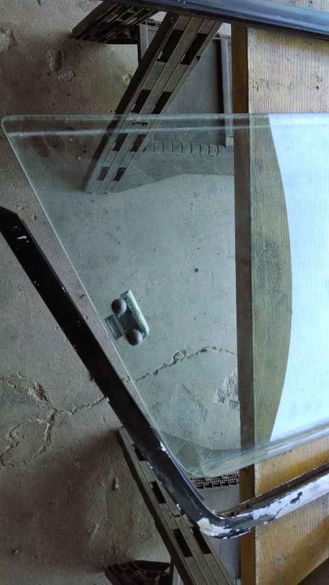 1992 Ford Bronco - A triangular piece of automotive glass, likely a vent window, is shown resting on a concrete surface with a black metal frame attached. A s…