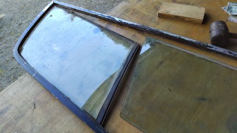 1992 Ford Bronco - Two pieces of glass, likely from a vehicle window, are laid out on a wooden surface. One piece is still in a dark metal frame, while the ot…