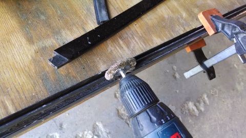 1992 Ford Bronco - A wire brush attached to a drill is being used to clean a black metal channel or trim piece that is clamped to a wooden surface. Another pi…