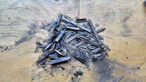 1992 Ford Bronco - A pile of broken charcoal sticks and dust scattered on a wooden surface.