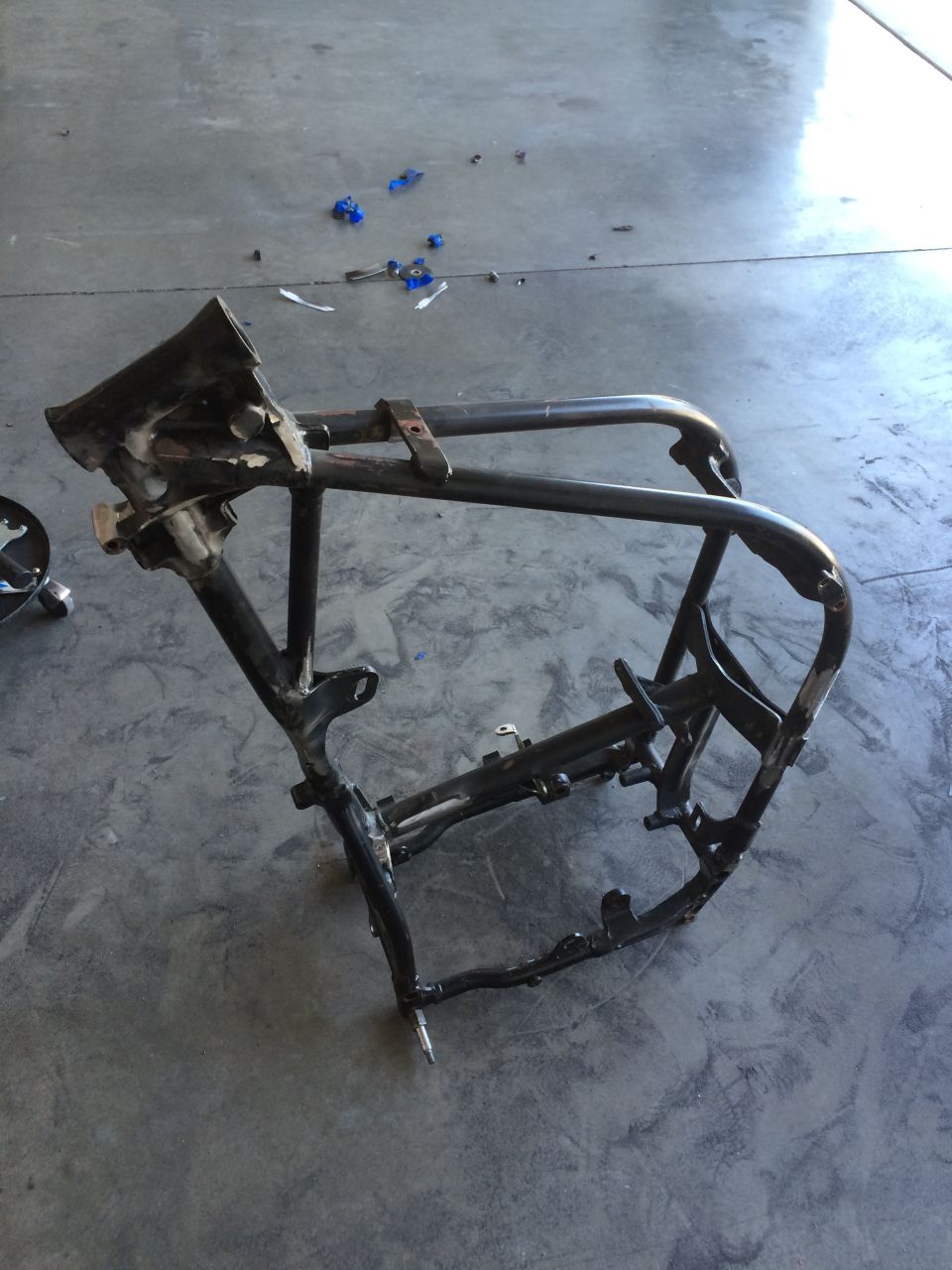 Black motorcycle frame on a concrete floor with blue debris.