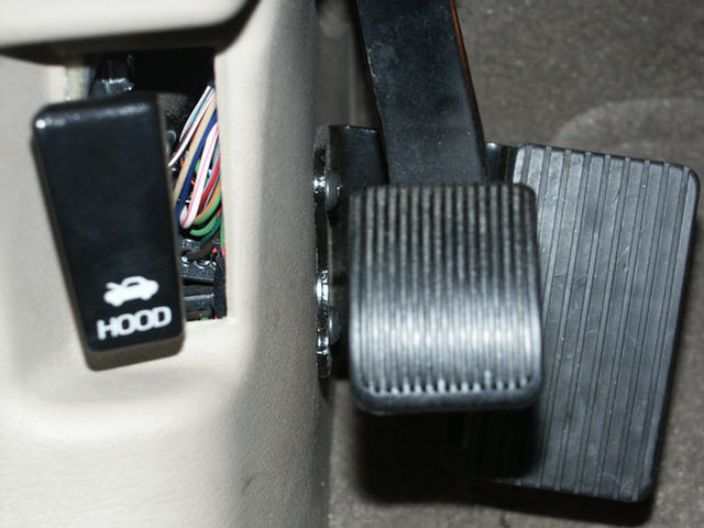 Interior footwell with black brake pedal and HOOD release lever on tan trim, wiring visible