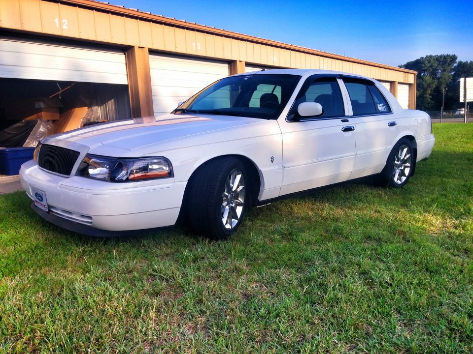 White Mercury Grand Marquis parked on grass in front of garage, front view